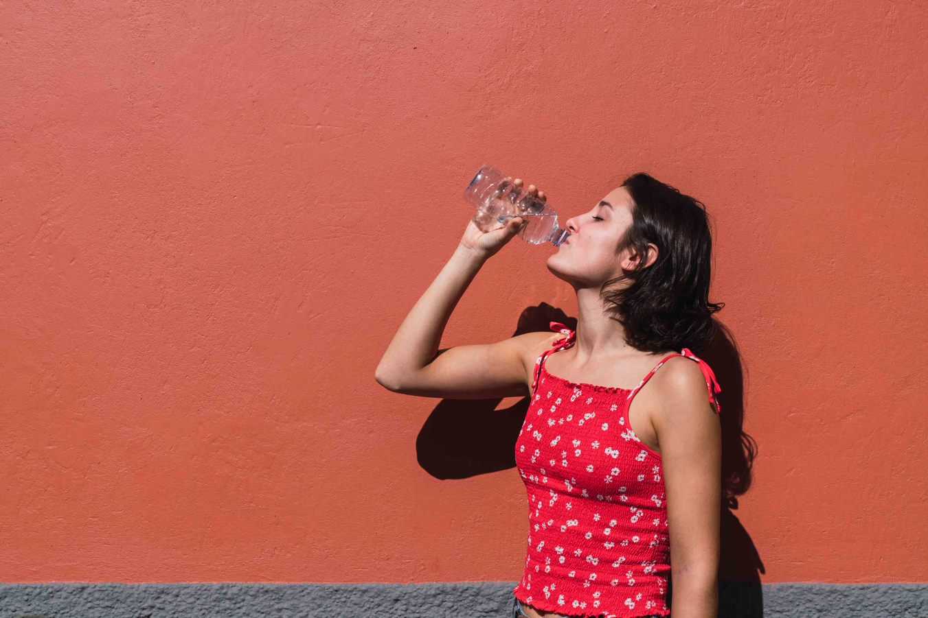 woman drinking water on red wall
